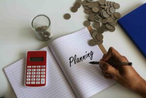 Young people planning savings with a notebook, calculator, and money jar to build healthy financial habits